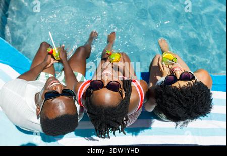 Three tropical cocktails resting on striped towel at pool edge with bright sun reflections Stock Photo