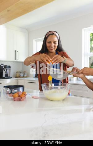 Egg yolks and whites passing through metal sieve into glass mixing bowl on marble island, sunlight Stock Photo