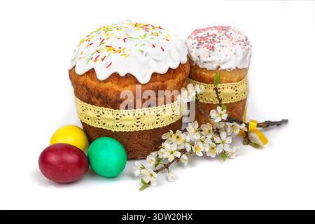 A cake with frosting and sprinkles stands beside colorful eggs and spring blossoms for an Easter celebration during the holiday. Stock Photo