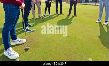 Groups of new golfers practice putting on the green during a sunny day, focusing on techniques and gaining confidence in their skills. Stock Photo