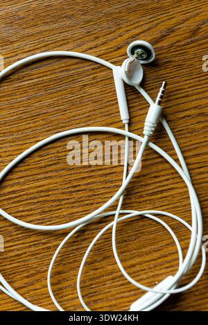 Messy white earbuds with cable lying on a brown wood table background representing modern audio accessories and technology Stock Photo