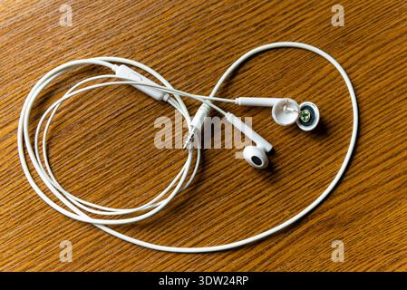 Neatly circular coiled white wired headphones on a brown wooden background depicting audio equipment and portable sound Stock Photo
