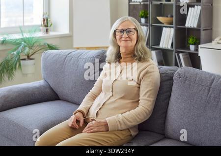 Happy confident senior woman sitting on home sofa in relaxing pose to enjoy carefree day with smile Stock Photo
