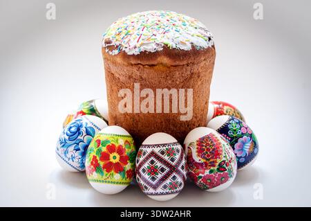 Easter Kulich Cake with Sugar Icing and Sprinkles Surrounded by Colorful Ukrainian Pysanky Eggs on White Background, Festive Spring Tradition, Bright Stock Photo