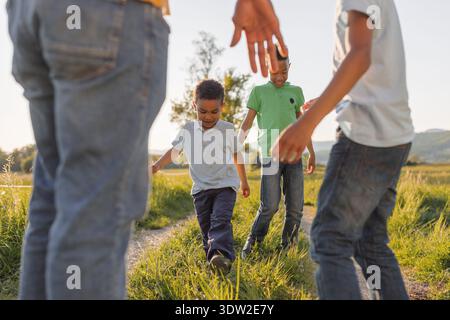 Single father walks with his two sons in a green field as they share joyful moments during sunset. Stock Photo