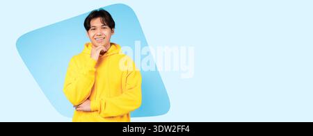 Young Man Smiles in Yellow Hoodie Against Blue Background With a Friendly Expression on His Face Stock Photo