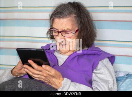 Elderly woman using tablet at home, relaxed senior reading and enjoying digital technology Stock Photo