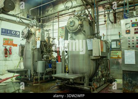 Detailed view of vintage industrial machinery in a processing plant with retro control panels, pipes, and valves under warm lighting. Stock Photo