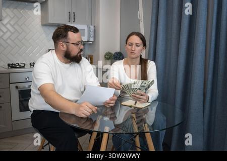 Young adult couple discussing their financial issues at home, counting cash and reviewing documents, experiencing stress while managing income and exp Stock Photo