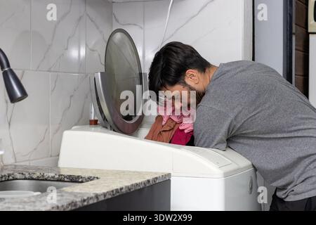 A young man putting clothes in the washing machine Stock Photo