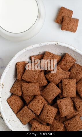 Chocolate pads in a white plate on a marble table and a glass of milk. A delicious and healthy breakfast. Selective focus, top view Stock Photo