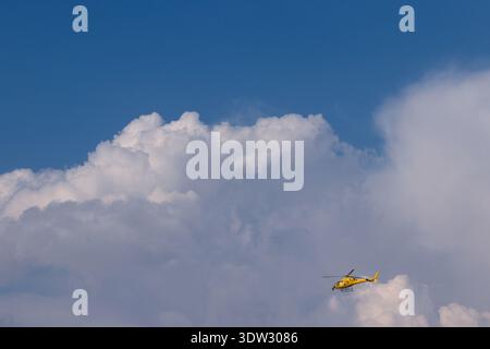 ALANYA, TURKEY -  November 09.2018:A bright yellow helicopter flies across a dramatic sky filled with towering cumulus clouds and soft blue tones, evo Stock Photo