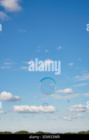 Rainbow-colored soap bubble floating against a beautiful blue sky with white clouds. Stock Photo