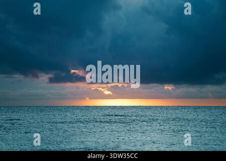 Dramatic dark rain clouds gather over the open Atlantic Ocean at dawn. This moody seascape depicts the approaching storm. Stock Photo