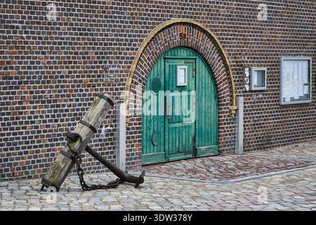 Historic wooden stock anchor with iron flukes in front of a green wooden door on a brick wall at Stralsund harbor Stock Photo
