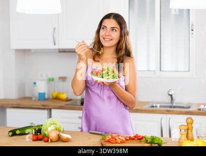 Smiling young woman eating salad at home Stock Photo