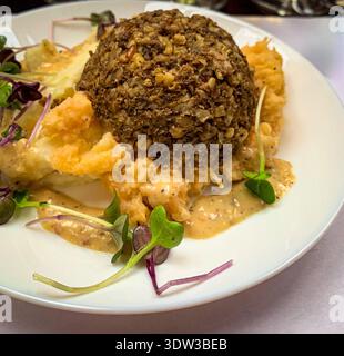 A mound of classic Scottish haggis served atop mashed yellow turnips and mashed potatoes (neeps and tatties) on a white plate. Stock Photo