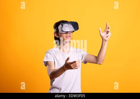 Focused male gamer with vr headset, interacting with invisible 3D objects in augmented reality simulation. Young man enjoys immersive entertainment, fully engaged in futuristic virtual environment. Stock Photo