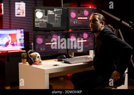 Hacker in hideout preparing to escape before getting caught after being found by police while writing malware code on computer. Man in criminal den found by anti hacking law enforcement Stock Photo