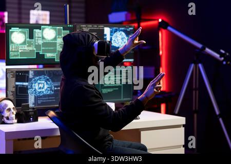 Hacker in secret lair using virtual reality tech and AI to break into secure computer systems and bypass security. Rogue programmer wearing VR headset uses deep learning to attack company networks Stock Photo