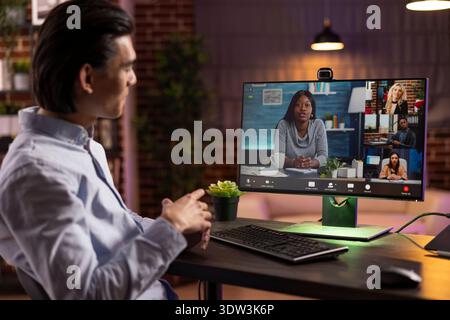 Male entrepreneur joins virtual discussion with multiethnic colleagues to plan marketing projects. Self employed man works from home, sharing business updates with shareholders on video conference. Stock Photo