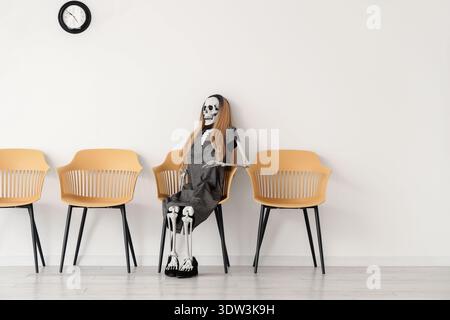 Human skeleton model with wig in chair near light wall Stock Photo