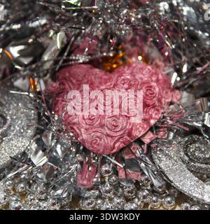 A pink heart with rose patterns surrounded by shiny silver tinsel. Scene conveys a festive atmosphere, suitable for celebrations or romantic occasions Stock Photo