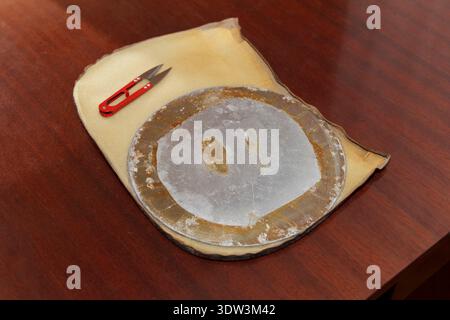Overhead view of a workshop. A worn circular sanding disc and red thread snips rest on a foam pad on a dark brown wooden table. Industrial, rustic aes Stock Photo