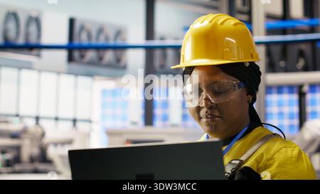 Specialist using laptop to conduct routine inspections in industry 4.0 plant producing renewable energy. Technician in photovoltaics smart factory testing equipment using notebook, camera B Stock Photo