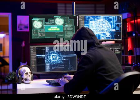Hooded hacker typing on PC keyboard, using AI to break into secure computer systems and bypass security. Rogue engineer uses neural networks to attack weak spots in company networks Stock Photo