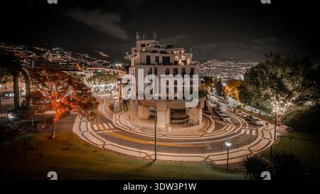 Dramatic nighttime urban scene centered on a circular building and roundabout, in Funchal, Madeira island, Portugal Stock Photo