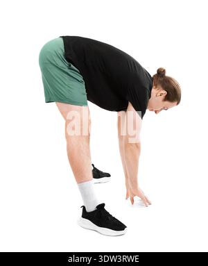 Sporty young man with long hair stretching his hamstrings by bending forward to touch the floor. Athletic male in green shorts isolated on white backg Stock Photo