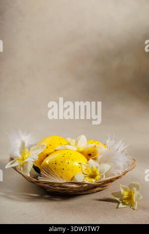 Easter basket with yellow speckled eggs, daffodils and white feathers vertical composition Stock Photo