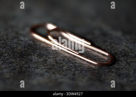 Selective focus macro shot of a single copper-colored paperclip on a dark textured background Stock Photo