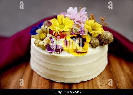 Elegant white cream cake decorated with vibrant colorful edible flowers Stock Photo