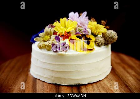 Elegant white cream cake decorated with vibrant colorful edible flowers Stock Photo