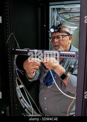 Adult technician working inside a server rack cabinet connecting and terminating network cables. The image represents data infrastructure, telecommuni Stock Photo