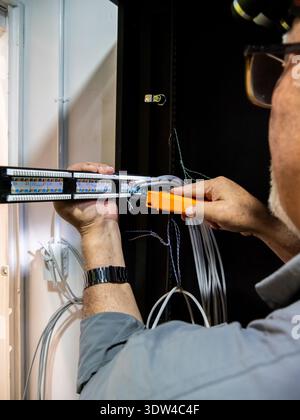 Adult technician working inside a server rack cabinet connecting and terminating network cables. The image represents data infrastructure, telecommuni Stock Photo