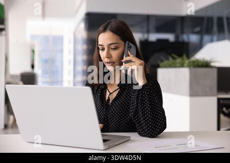 Multitasking female professional talking on cellphone and typing on laptop Stock Photo