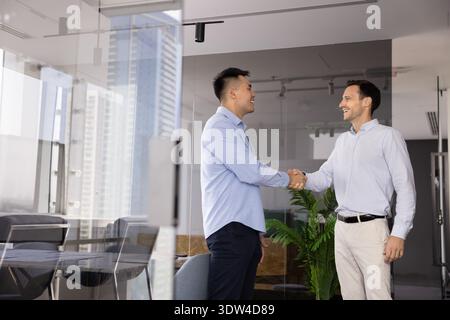 Happy confident diverse male entrepreneurs shaking hands in glass office Stock Photo