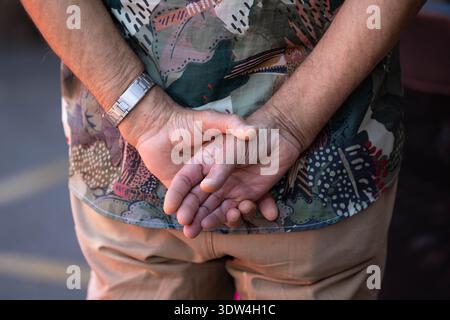 Man's hands clasped behind back, unposed movement, natural candid motion, hand skin and nail texture, close-up, at Chatuchak Market. Stock Photo
