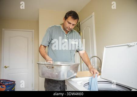 Middle aged man doing laundry at home loading clothes into washing machine during daily household routine Stock Photo