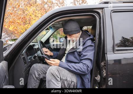 Farmer using smartphone while sitting in pickup truck during autumn vineyard work Stock Photo