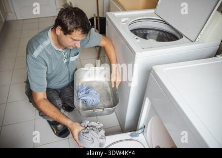 Middle aged man sorting laundry and loading clothes into washing machine at home performing daily household chores in laundry room Stock Photo