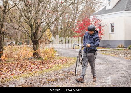 Man carrying bicycle on muddy road after rain in autumn Stock Photo