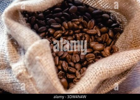 Close-up of roasted coffee beans overflowing from a rustic jute sack, highlighting rich texture and warm brown tones Stock Photo