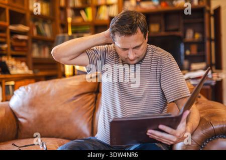 Man reviewing documents with worried expression while sitting on sofa at home Stock Photo