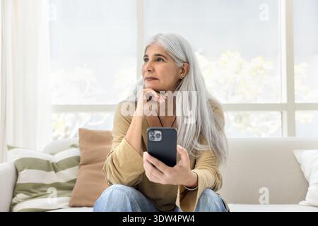 Woman holding smartphone, gazing into distance in thoughtful mood Stock Photo