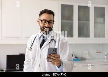 Smiling male doctor text message on phone in health app Stock Photo