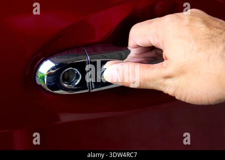 Secure Keyless Car Entry, A hand reaches to press the black button on a chrome car door handle to unlock a red vehicle using keyless entry technology. Stock Photo